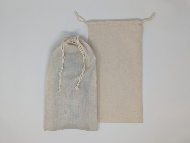 May include: Two off-white drawstring bags. One bag is closed with a drawstring, and the other is open. The bags are made of a natural-colored fabric. The closed bag appears to contain items, while the other is empty.