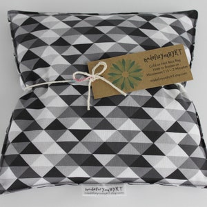 May include: A black and white geometric patterned pillow filled with rice for hot or cold therapy. The pillow is tied with twine and a tag that reads "madeforyouBYKT" and includes instructions for use.