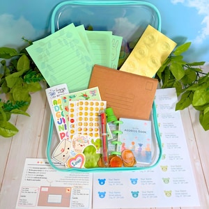 May include: A clear plastic zipper box containing stationery supplies including light green lined paper, a brown envelope, gold wax seals, colorful sticker sheets, a small address book, a multi-color pen, and printed address label sheets.
