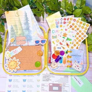 May include: A clear, yellow-trimmed stationery kit filled with summer-themed stickers, stationery, and an address book. Includes a brown envelope, a pen, and a sheet of address labels. The kit is decorated with summer camp and sunshine motifs.