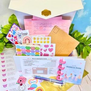 May include: A white stationery box containing pink lined paper, brown envelopes, sticker sheets with hearts, rainbows, and emojis, a multi-colored pen, and a small address book. A printed instruction card titled How to send your Letter is included.
