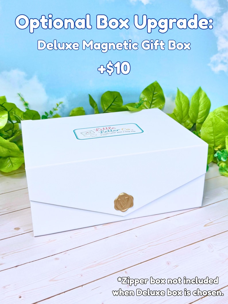 May include: A white rectangular magnetic gift box featuring a gold-colored wax seal on the front flap and a rectangular label on the lid that reads Little Letter Co. a little letter goes a long way. The box is presented against a light blue sky background.