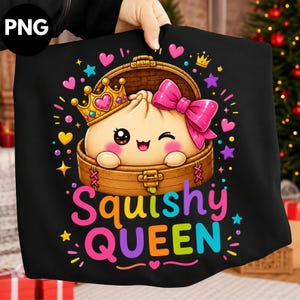 May include: A black t-shirt featuring a graphic of a cute, winking dumpling character inside a bamboo steamer basket. The dumpling wears a gold crown and a large pink bow. Below the basket, the text reads Squishy QUEEN in colorful letters.