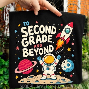 May include: A black t-shirt featuring a colorful space-themed graphic with the text "TO SECOND GRADE AND BEYOND". The design includes an astronaut standing on a cratered moon, a rocket ship launching, a ringed planet, and scattered stars.