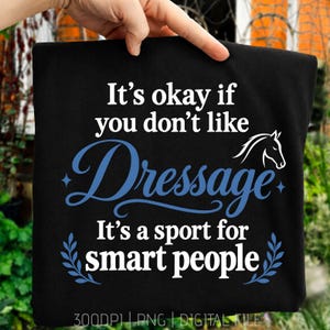 以下が含まれることがあります： 「It's okay if you don't like Dressage It's a sport for smart people」という白と青の文字がプリントされた黒いTシャツ。デザインには、白い馬の頭のシルエット、青い装飾的な模様、小さな四芒星のアクセントが含まれています。