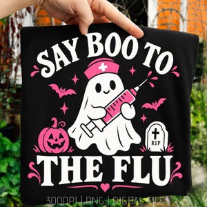 Könnte beinhalten: Ein schwarzes T-Shirt mit einem weißen Geist, der eine rosa Krankenschwesterhaube trägt und eine rosa Spritze hält. Das Design zeigt einen rosa Kürbis, einen Grabstein mit RIP, Fledermäuse und den weißen Text SAY BOO TO THE FLU mit rosa Akzenten.