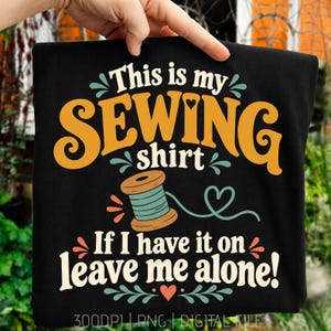 Pode incluir: Uma t-shirt preta com o texto "This is my SEWING shirt If I have it on leave me alone!" em amarelo, branco e azul-petróleo. O design inclui um gráfico de um carretel de linha azul-petróleo e corações, com "300DPI PNG DIGITAL FILE" na parte inferior.