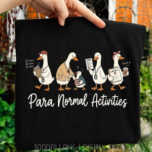 Puede incluir: Una camiseta negra con un gráfico de cuatro patos y un patito pequeño. Los patos visten ropa de oficina y sostienen portapapeles, un horario y una taza de café. El texto "Para Normal Activities" está impreso en blanco debajo de los patos.