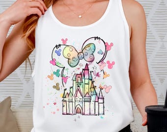 May include: A white sleeveless tank top featuring a colorful watercolor-style graphic of a castle and a large bow with mouse ears. The design includes scattered small mouse ear silhouettes in various pastel colors, creating a whimsical aesthetic.
