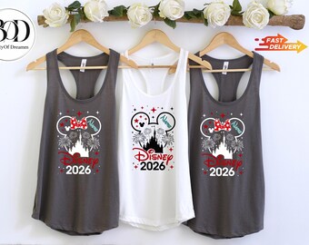 May include: Two dark gray and one white racerback tank top, each featuring a graphic of a castle silhouette, fireworks, and a mouse-ear outline with a red polka-dot bow. The text reads Disney 2026 with a space for a name in blue script.