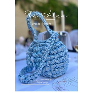 Può includere: Una borsa all'uncinetto azzurra con un manico intrecciato spesso e un corpo arrotondato e testurizzato. L'immagine presenta il testo The Alex Crochet Pattern e Handmade by Rayray. La borsa è realizzata con un filato liscio simile a un nastro.