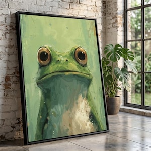 Puede incluir: Una impresión artística enmarcada con una ilustración caprichosa de una rana. La rana tiene ojos marrones grandes y expresivos y está pintada en tonos verdes y beige sobre un fondo verde claro. La obra de arte se presenta en un marco negro.