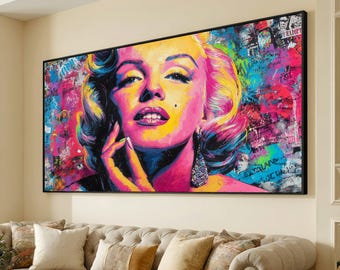 May include: A vibrant pop art style portrait of Marilyn Monroe. The artwork features a colorful background with graffiti-style elements. The portrait is framed in black and hangs above a beige sofa with decorative pillows.