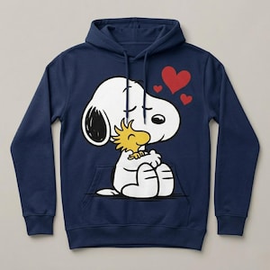May include: Navy blue hoodie featuring a graphic of Snoopy hugging Woodstock, with three red hearts above. The white Snoopy has black accents, and Woodstock is yellow. The hoodie has a front pocket and a drawstring hood.