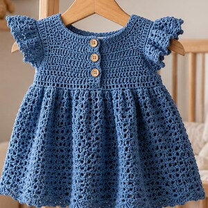 May include: A blue crochet dress featuring a round neckline, short ruffled sleeves, and a button-down front closure with three light brown wooden buttons. The bodice is worked in a dense stitch, while the skirt features an openwork pattern.