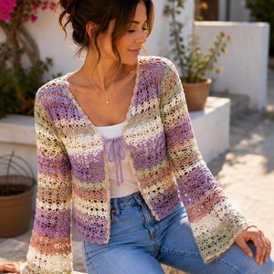 Puede incluir: Un cárdigan de ganchillo de manga larga con apertura frontal, que presenta una paleta de colores variados en lavanda, verde salvia, crema y rosa suave. La prenda tiene un delicado patrón de punto calado, cuello en V y un fino lazo a juego.