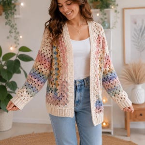 May include: A cream-colored, open-front crochet cardigan with pastel rainbow squares on the sleeves and body. The cardigan has a classic granny square design and ribbed cuffs. The model is wearing blue jeans and a white top.
