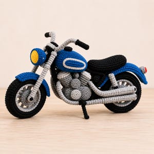 Peut inclure: Moto crochetée en bleu, noir, gris et jaune. Ce jouet fait main présente un réservoir bleu avec une bande blanche, une selle noire et des composants de moteur gris. Les roues sont noires avec des rayons gris et le phare est jaune.