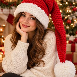 Könnte beinhalten: Eine lange, gehäkelte Weihnachtsmannmütze in Rot mit einem dicken, weißen, strukturierten Rand und einem großen, flauschigen weißen Bommel an der Spitze. Die Mütze besteht aus einem dichten Garnmaterial mit einem sichtbaren Maschenmuster.