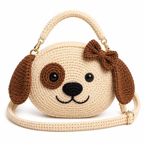 Puede incluir: Un bolso de mano redondo de ganchillo en color crema con forma de cara de cachorro. Presenta orejas caídas marrones, una mancha marrón en el ojo, nariz negra, una sonrisa bordada y un pequeño lazo marrón. Incluye asa superior y correa larga.