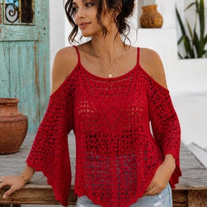 Puede incluir: Un top de crochet rojo con hombros descubiertos y mangas largas acampanadas. El top presenta un diseño delicado de tejido abierto y finas correas de espagueti. La prenda se combina con pantalones cortos de mezclilla. El top es de un tono rojo vibrante.