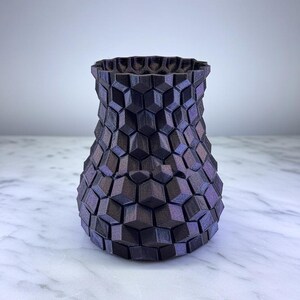 Könnte beinhalten: Eine dunkelviolette Vase mit einem geometrischen Wabenmuster. Die Vase hat einen breiten Boden, der sich zu einem schmaleren Hals verjüngt, und eine strukturierte Oberfläche. Die Vase besteht aus einem 3D-gedruckten Material.