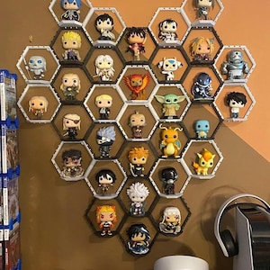May include: A wall-mounted display of Funko Pop figures arranged in a honeycomb pattern. The figures are of various characters, with a variety of colors and designs. The display is made of black and white hexagonal shelves. The wall is painted a warm brown.