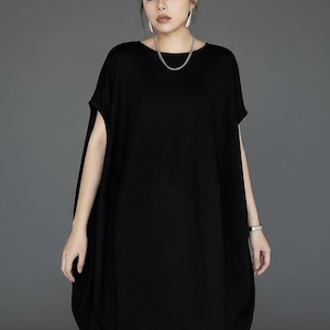 Può includere: Un abito nero oversize con maniche corte e una silhouette arrotondata unica. L'abito presenta un design semplice e minimalista, perfetto per un look casual ma elegante. La modella indossa una collana e un braccialetto d'argento.