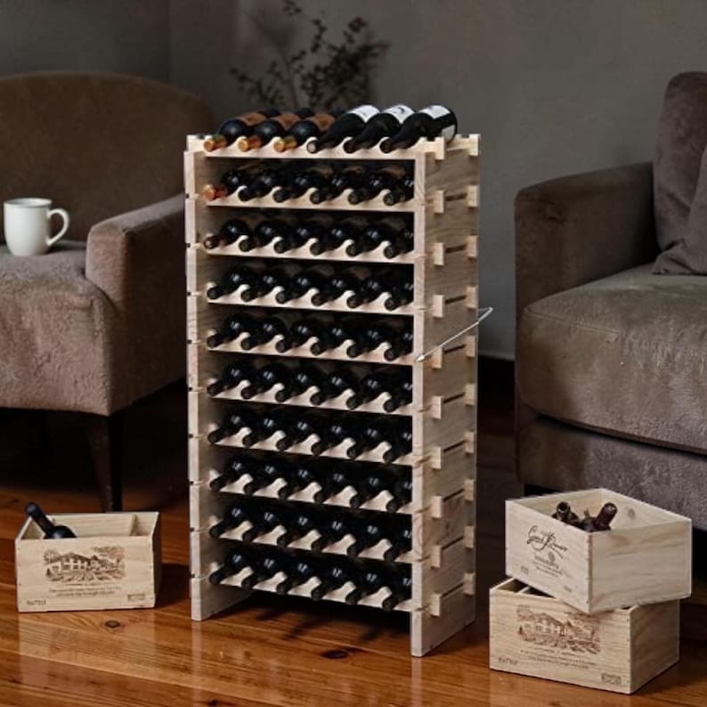 May include: A tall, light-colored wooden wine rack filled with wine bottles. The rack has multiple shelves and is surrounded by two wooden crates. The wine rack is in a living room setting with a couch and chair.