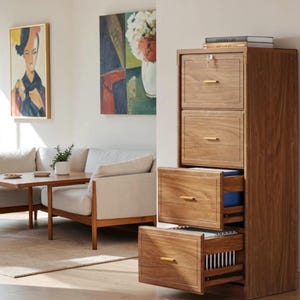 May include: A tall, four-drawer wooden filing cabinet with a natural wood grain finish. The cabinet features slim, horizontal gold-toned metal handles on each drawer front. The top drawer includes a silver-colored key lock mechanism.