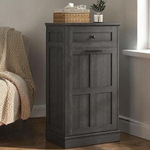 May include: A dark gray wooden cabinet with a drawer and a door. A woven basket and a small plant in a glass vase sit on top. The cabinet has a rectangular shape and is made of wood.