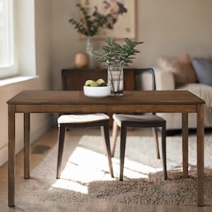 Puede incluir: Una mesa de comedor rectangular de madera marrón oscuro con dos sillas. La mesa está decorada con un cuenco blanco de fruta y un jarrón con vegetación. Las sillas tienen asientos tapizados. La mesa mide aproximadamente 150 cm de largo.