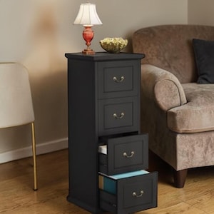 May include: A black, four-drawer file cabinet with brass-colored handles. The top of the cabinet has a small lamp with a white shade and a decorative bowl. Two drawers are open, revealing files. The cabinet is in a room with a chair and a sofa.