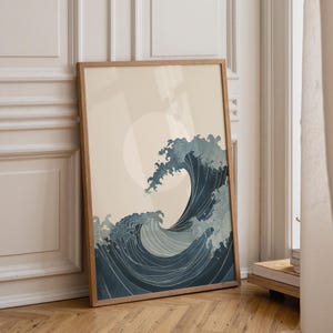 May include: A framed art print featuring a stylized depiction of a large ocean wave in shades of blue and white, with a circular sun in the background. The artwork is in a wooden frame and leans against a wall.