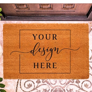 May include: A rectangular doormat made of a natural brown material. The mat features a black rectangular border with the words "YOUR design HERE" in a black, elegant font. The mat is placed in front of a door.