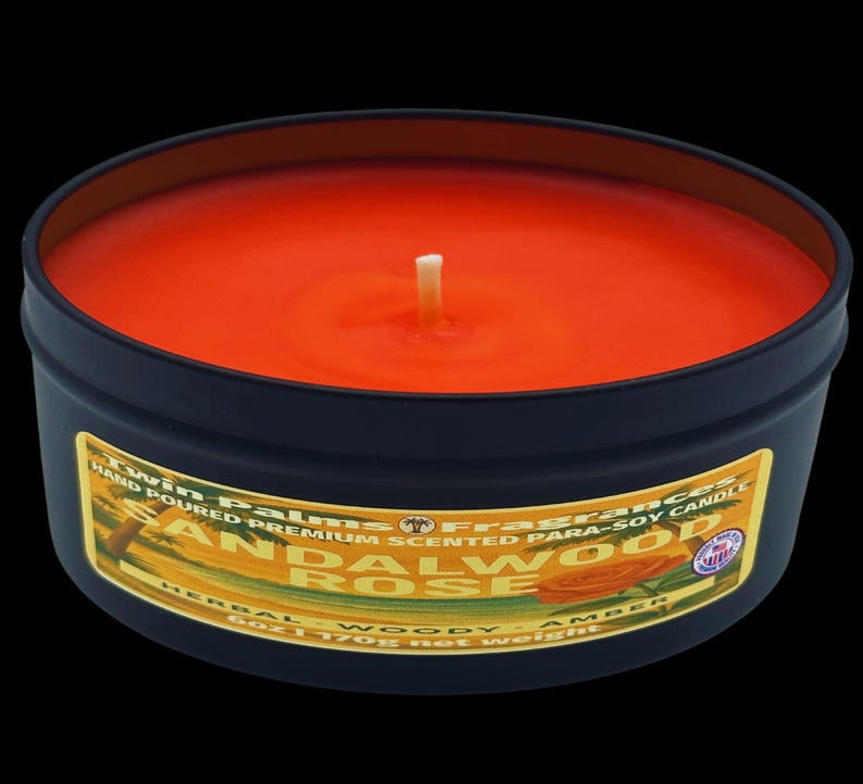 A round, black candle tin with an orange-colored wax and a white wick. The label reads "Sandalwood Rose" and "Hand Poured Premium Scented Para-Soy Candle". The candle weighs 6 oz (170g).
