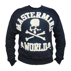 May include: Navy blue sweatshirt with a white skull and crossbones graphic, and the text "MASTERMIND WORLD". The design is centered on the chest. The sweatshirt has a crew neck and long sleeves.