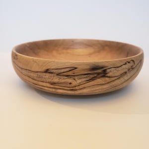 Puede incluir: Un cuenco de madera hecho a mano con un acabado natural. El cuenco es de color marrón claro con vetas marrones oscuras. Tiene forma redonda con una amplia abertura, adecuado para servir o exhibir. Diámetro: aproximadamente 25 cm.