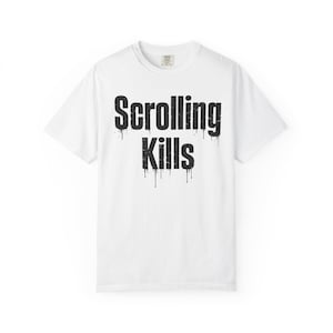 May include: White t-shirt with the text "Scrolling Kills" in large, black, dripping font. The shirt has a crew neck and short sleeves. The text is centered on the front of the shirt.