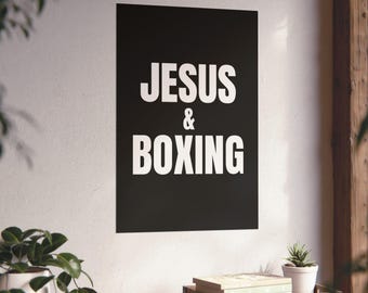 Puede incluir: Un póster de pared rectangular con un fondo negro sólido y el texto blanco JESUS & BOXING impreso en una fuente sans-serif en negrita. El póster se muestra verticalmente en una pared lisa, exhibiendo una tipografía clara y contrastada.