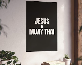 Puede incluir: Un póster de pared rectangular negro que presenta el texto blanco JESUS & MUAY THAI centrado en una fuente sans-serif en negrita. El póster se muestra verticalmente sobre una pared blanca lisa, ofreciendo una presentación visual contrastada.