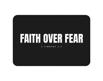Puede incluir: Una alfombrilla rectangular negra con el texto blanco FAITH OVER FEAR en una fuente negrita sin remates. Debajo del texto principal, el texto blanco más pequeño 2 TIMOTHY 1:7 está centrado. La alfombrilla tiene esquinas redondeadas.