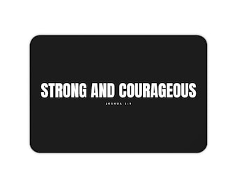 Puede incluir: Una alfombra rectangular negra con el texto blanco "STRONG AND COURAGEOUS" en una fuente sans-serif en negrita, con el texto blanco más pequeño "JOSHUA 1:9" centrado directamente debajo de la frase principal sobre un fondo negro.