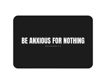 Puede incluir: Una alfombrilla rectangular negra con el texto blanco BE ANXIOUS FOR NOTHING en una fuente sans-serif en negrita, con el texto blanco más pequeño PHILIPPIANS 4:6 centrado directamente debajo de la frase principal en un estilo limpio.