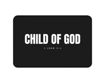 Puede incluir: Un tapete rectangular negro que presenta el texto blanco CHILD OF GOD en una fuente sans-serif en negrita centrada en la superficie. Debajo del texto principal, el texto blanco más pequeño 1 JOHN 3:1 está impreso, con esquinas redondeadas.