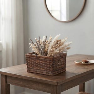 May include: A rectangular dark brown woven wicker basket filled with a variety of dried botanical stems, including fluffy pampas grass, lavender sprigs, and small seed pods, creating a textured arrangement of neutral and muted earth tones.