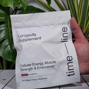 May include: A white packet labeled "Longevity Supplement" with the text "Cellular Energy, Muscle Strength & Endurance." The packet also includes the text "mitopure Urolithin A" and "60 Softgels I Dietary Supplement." The word "time-line" is printed vertically on the right side.