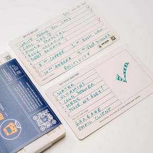 May include: Off-white index cards with handwritten daily routines and to-do lists. The cards include sections for tasks, times, and a weekly goal. One card has a checkmark graphic. The cards are part of a system for managing tasks.