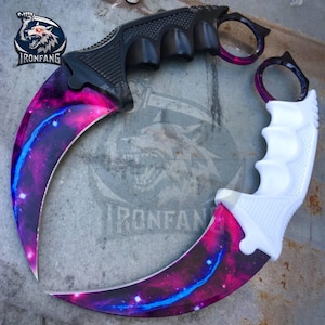 May include: Two curved karambit knives featuring blades with a vibrant purple, pink, and blue galaxy nebula pattern. One knife has a black handle with finger grooves and a ring pommel, while the other has a white handle with matching features.
