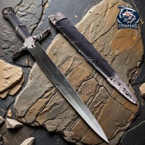 May include: A silver and black sword with a decorative handle and crossguard, resting on a stone surface. The sword has a long, sharp blade and is accompanied by a black sheath with silver accents. The Ironfang logo is visible in the upper right corner.